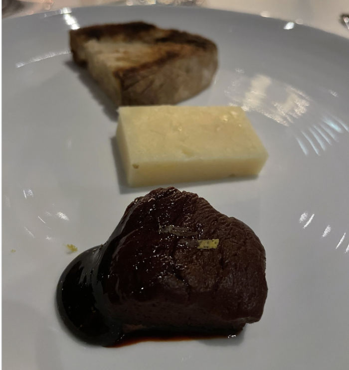 Bread, cheese, and dark quince on a white plate with concentric grooves in it.